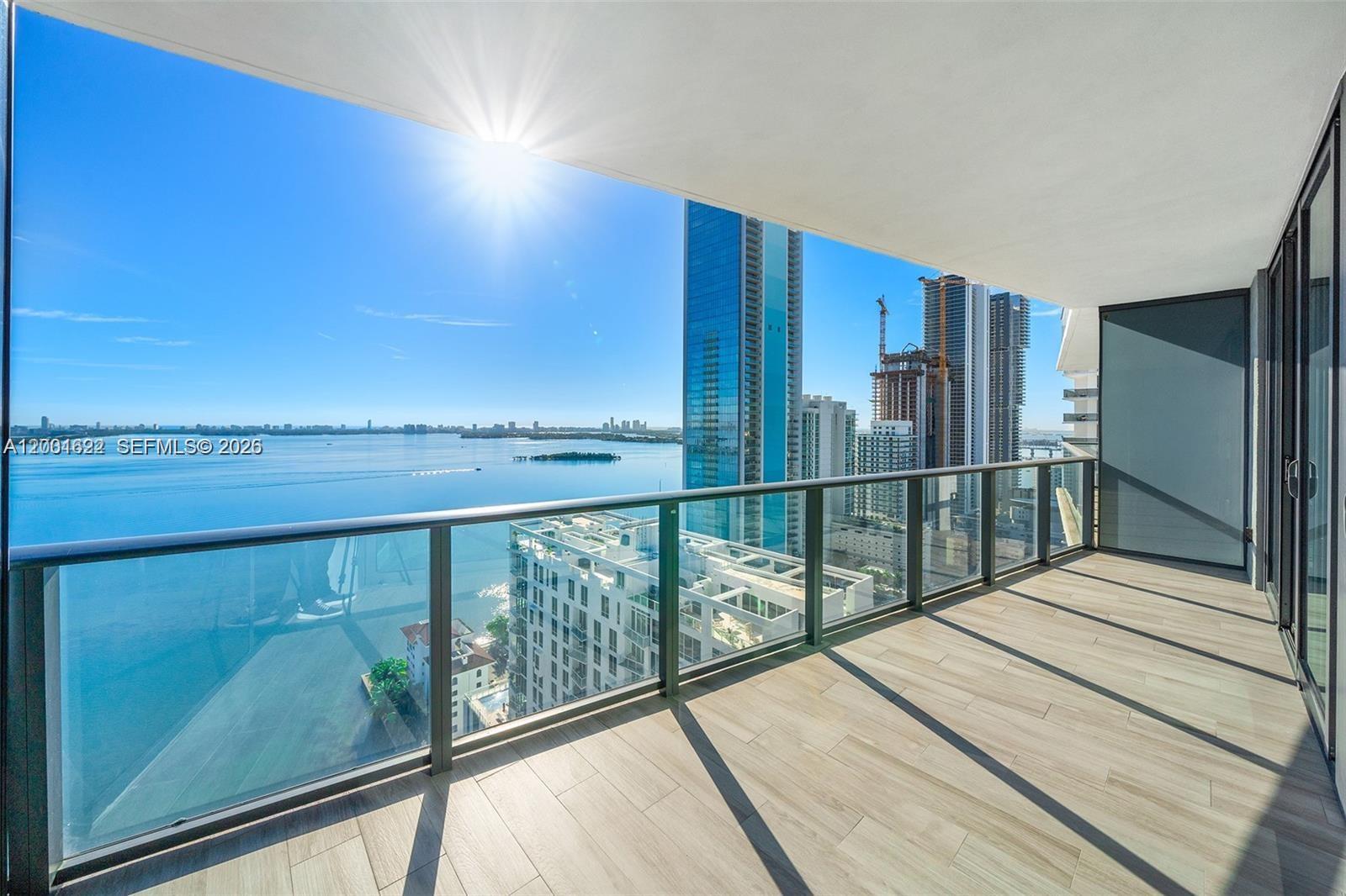 A high-rise balcony features glass railings, wood-look tile flooring, and panoramic views of the bay — 460 NE 28th St # 2707, Miami FL 33137, MIAMI, FL