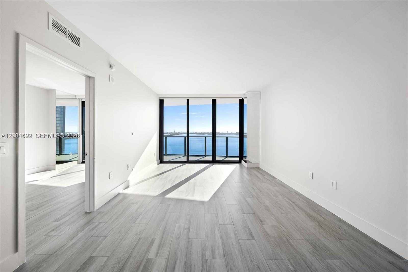 An empty room with light wood-look flooring, white walls, and a balcony overlooking the ocean — 460 NE 28th St # 2707, Miami FL 33137, MIAMI, FL