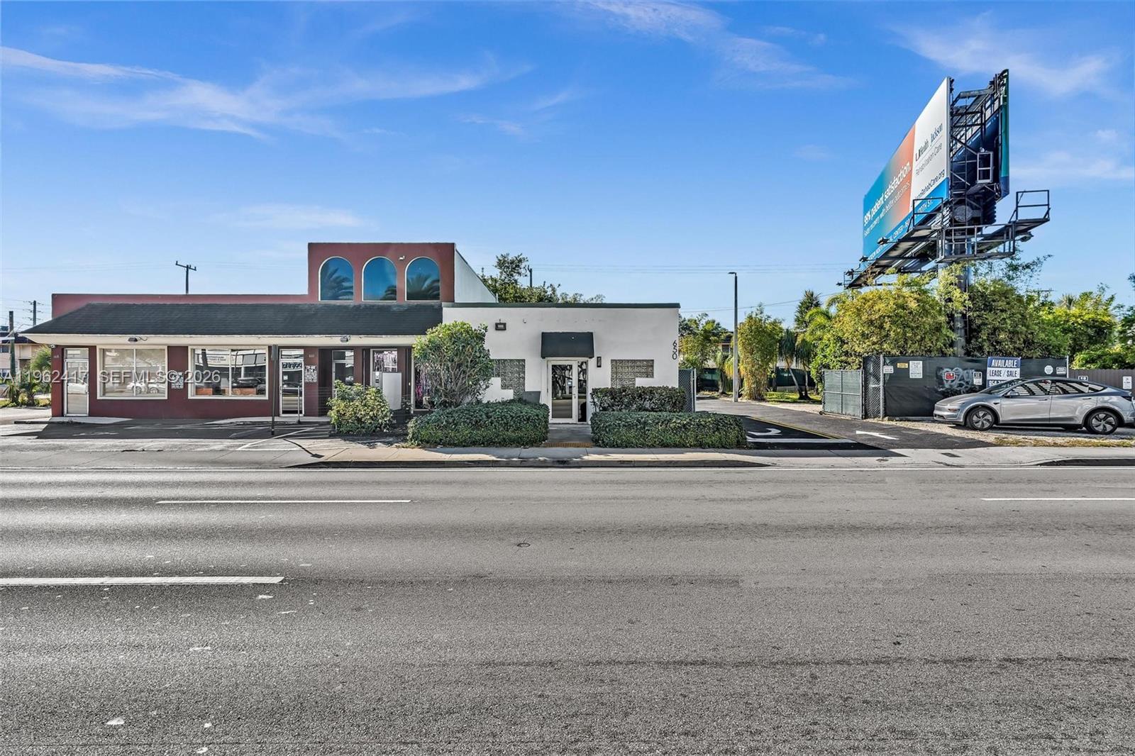 A commercial building with a red and white facade stands beside a large billboard — 650 NE 167th St, Miami FL 33162, MIAMI, FL