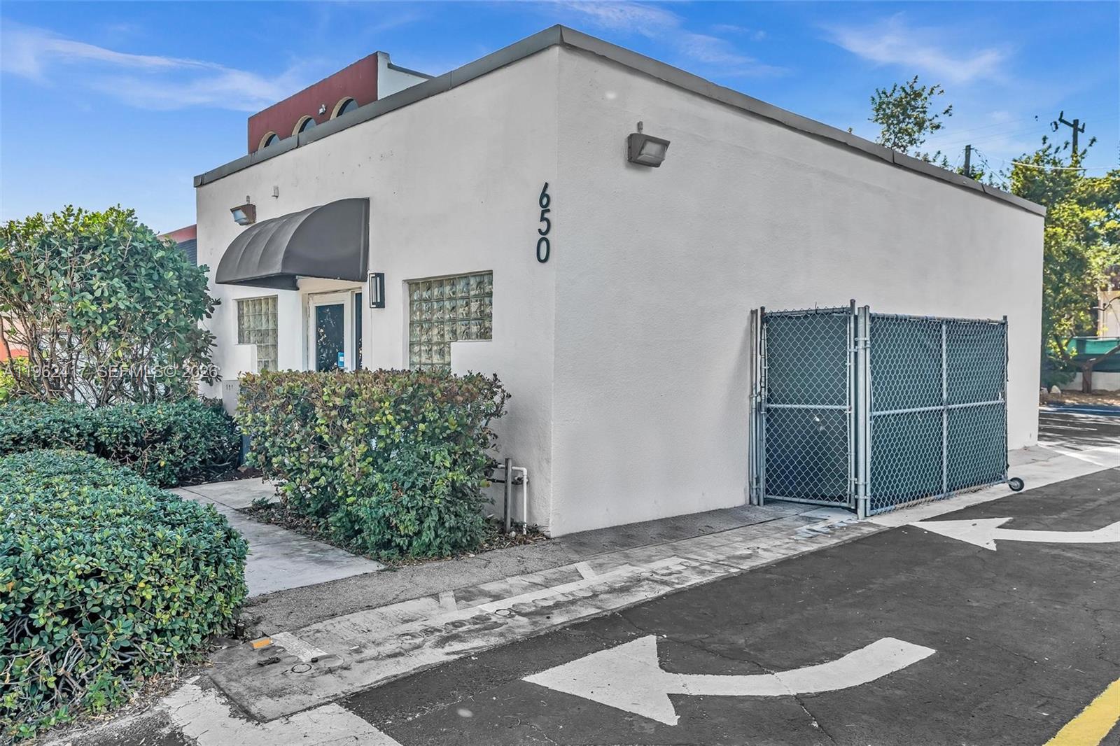 A white commercial building with a black awning, glass block windows, and a chain-link enclosure — 650 NE 167th St, Miami FL 33162, MIAMI, FL