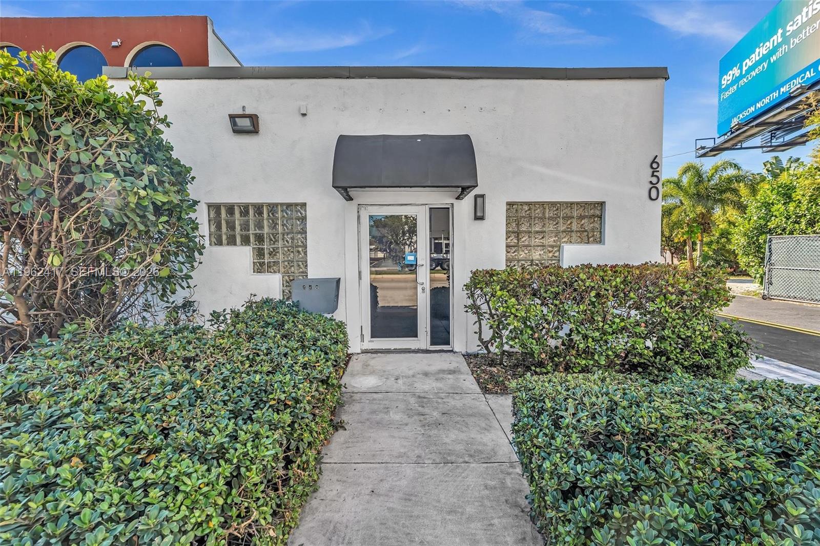 The exterior of a white commercial building features a glass door and glass block windows — 650 NE 167th St, Miami FL 33162, MIAMI, FL