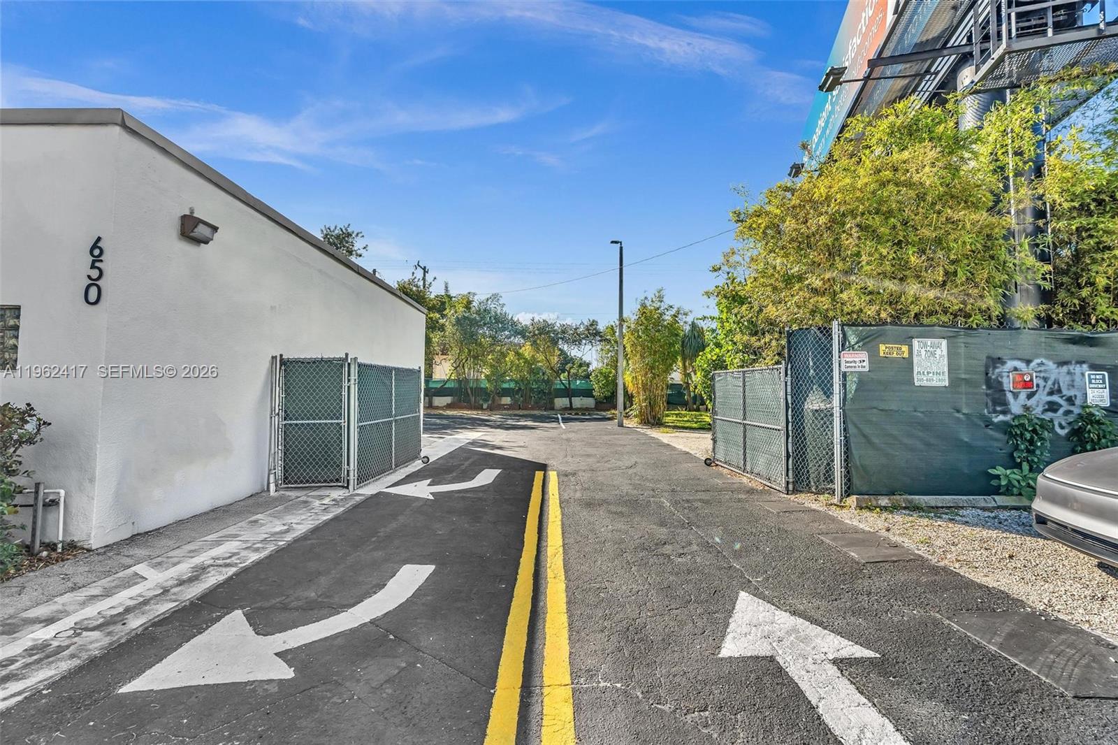 An outdoor paved driveway leads between a white building and a fenced area — 650 NE 167th St, Miami FL 33162, MIAMI, FL