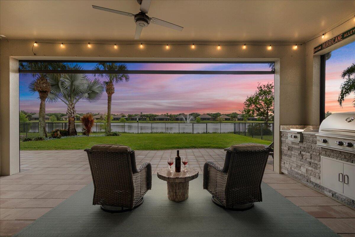 A covered patio features two chairs, a small table, and an outdoor kitchen overlooking a lake — 3704 Siena Circle, Wellington FL 33414, WELLINGTON, FL
