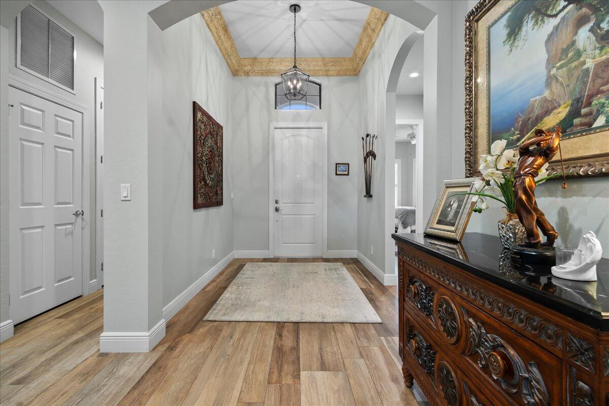 A foyer features light wood flooring, a tray ceiling with gold trim, and a chandelier — 3704 Siena Circle, Wellington FL 33414, WELLINGTON, FL