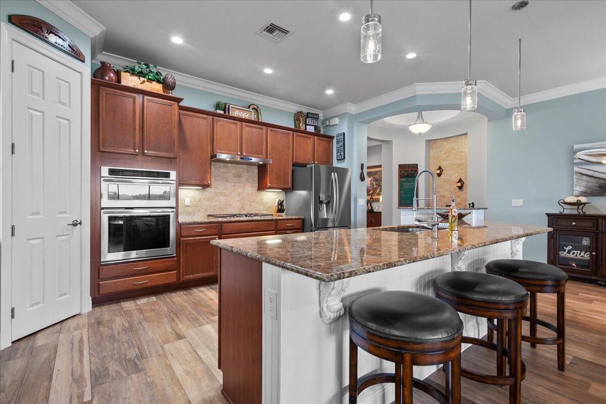 A kitchen features wood cabinets, granite countertops, a central island with stools, and light-blue walls — 3704 Siena Circle, Wellington FL 33414, WELLINGTON, FL
