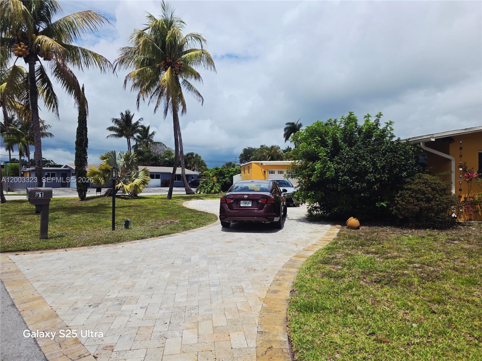 A paved driveway leads to a house with a parked car and palm trees — 31 NE 27th Dr, Wilton Manors FL 33334, WILTON MANORS, FL