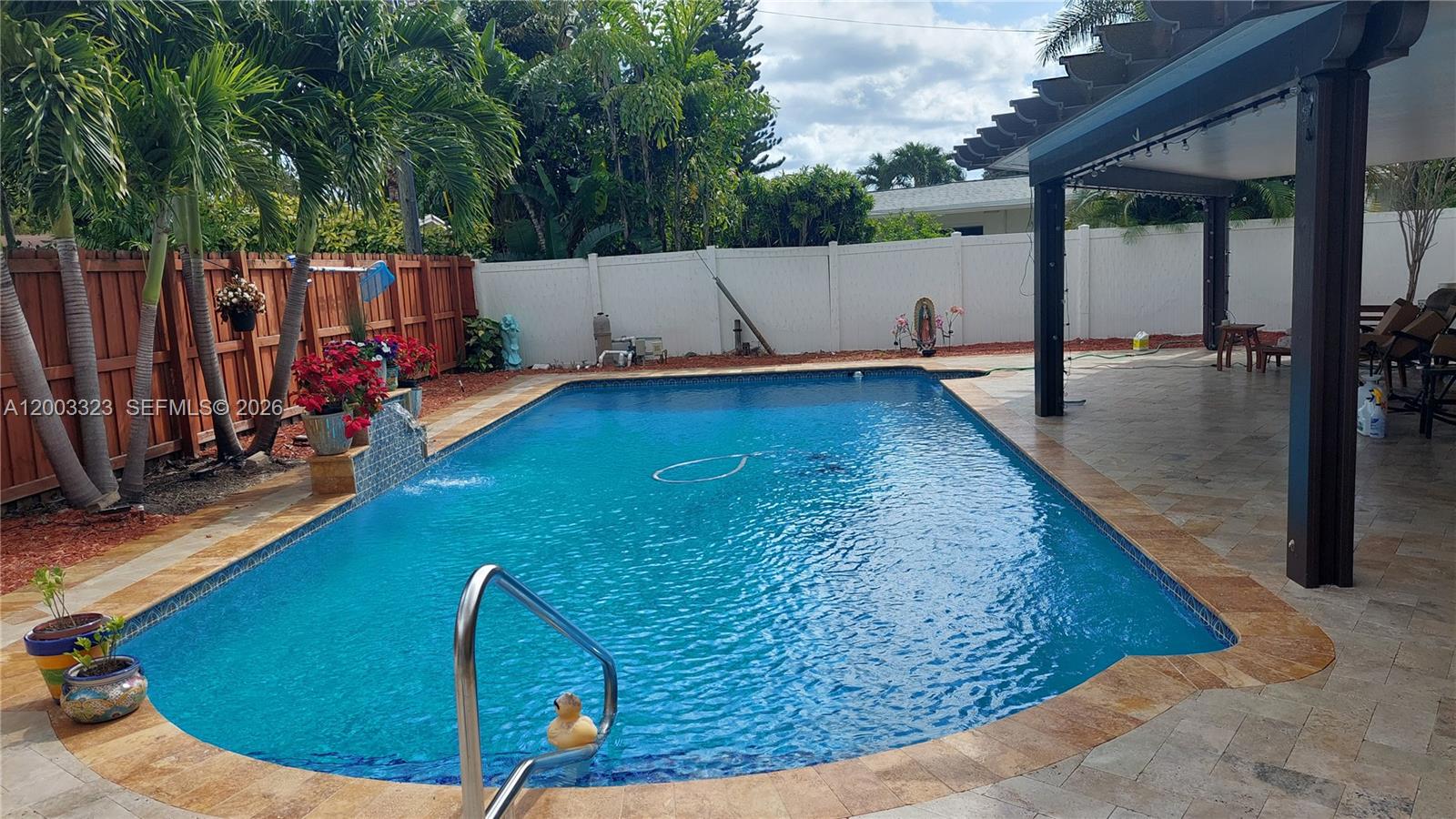 A backyard swimming pool with a stone deck, covered patio, and wooden privacy fence — 31 NE 27th Dr, Wilton Manors FL 33334, WILTON MANORS, FL