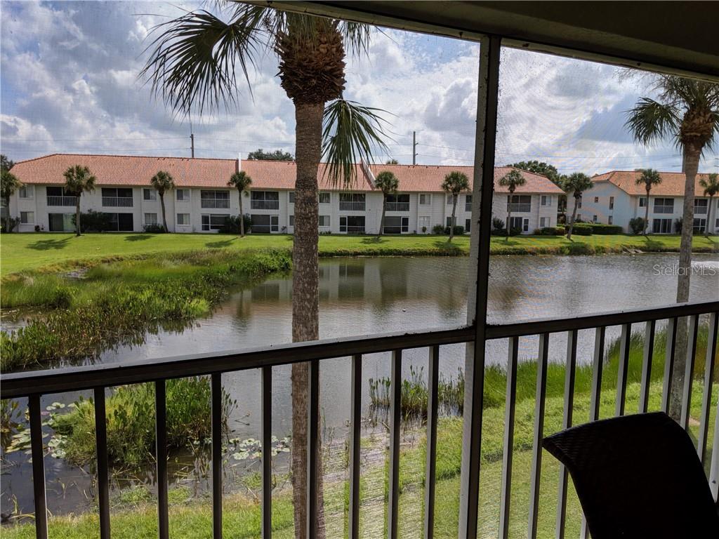 A view from a screened-in balcony overlooking a pond and apartment buildings with palm trees — 4378 MADERIA COURT COURT UNIT n/a, SARASOTA, FL