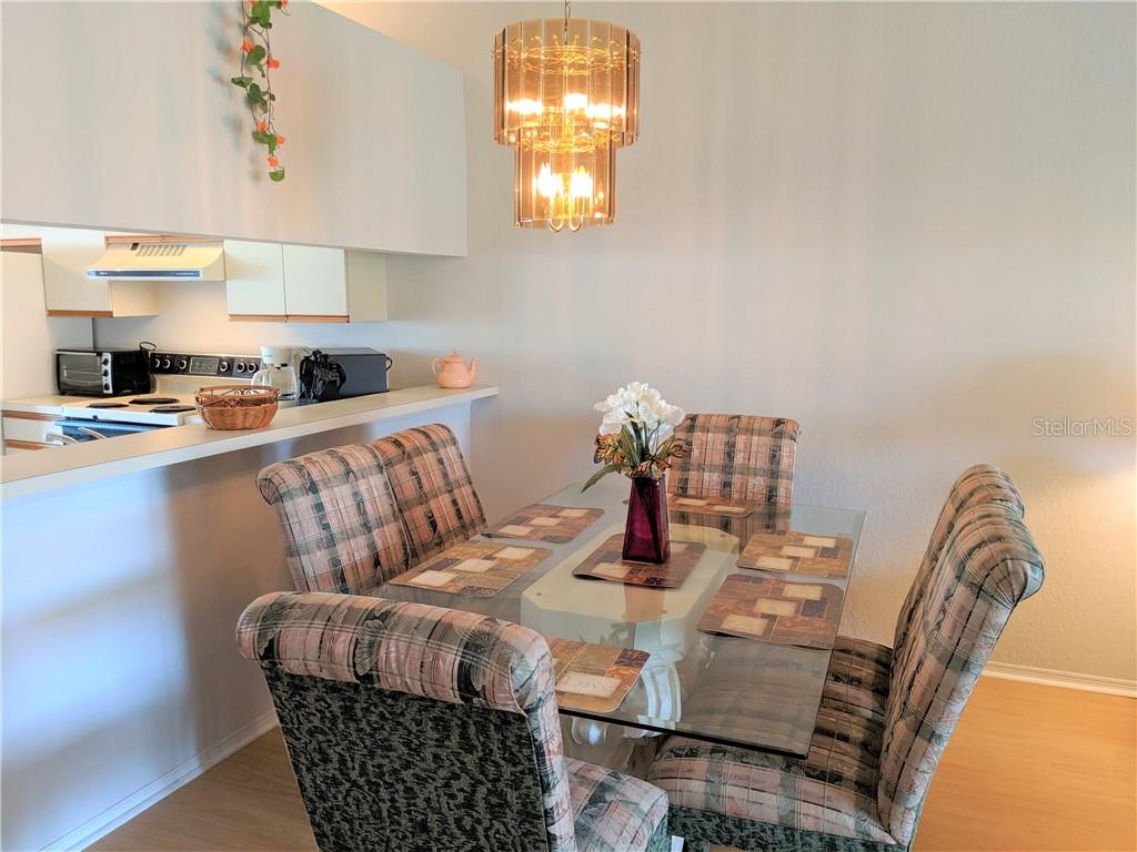 A dining area features a glass-topped table with plaid chairs beneath a tiered chandelier — 4378 MADERIA COURT COURT UNIT n/a, SARASOTA, FL
