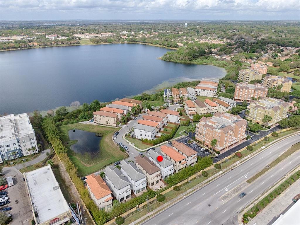 An aerial view shows a row of townhomes near a lake and a road — 7661 TOSCANA BOULEVARD, ORLANDO, FL