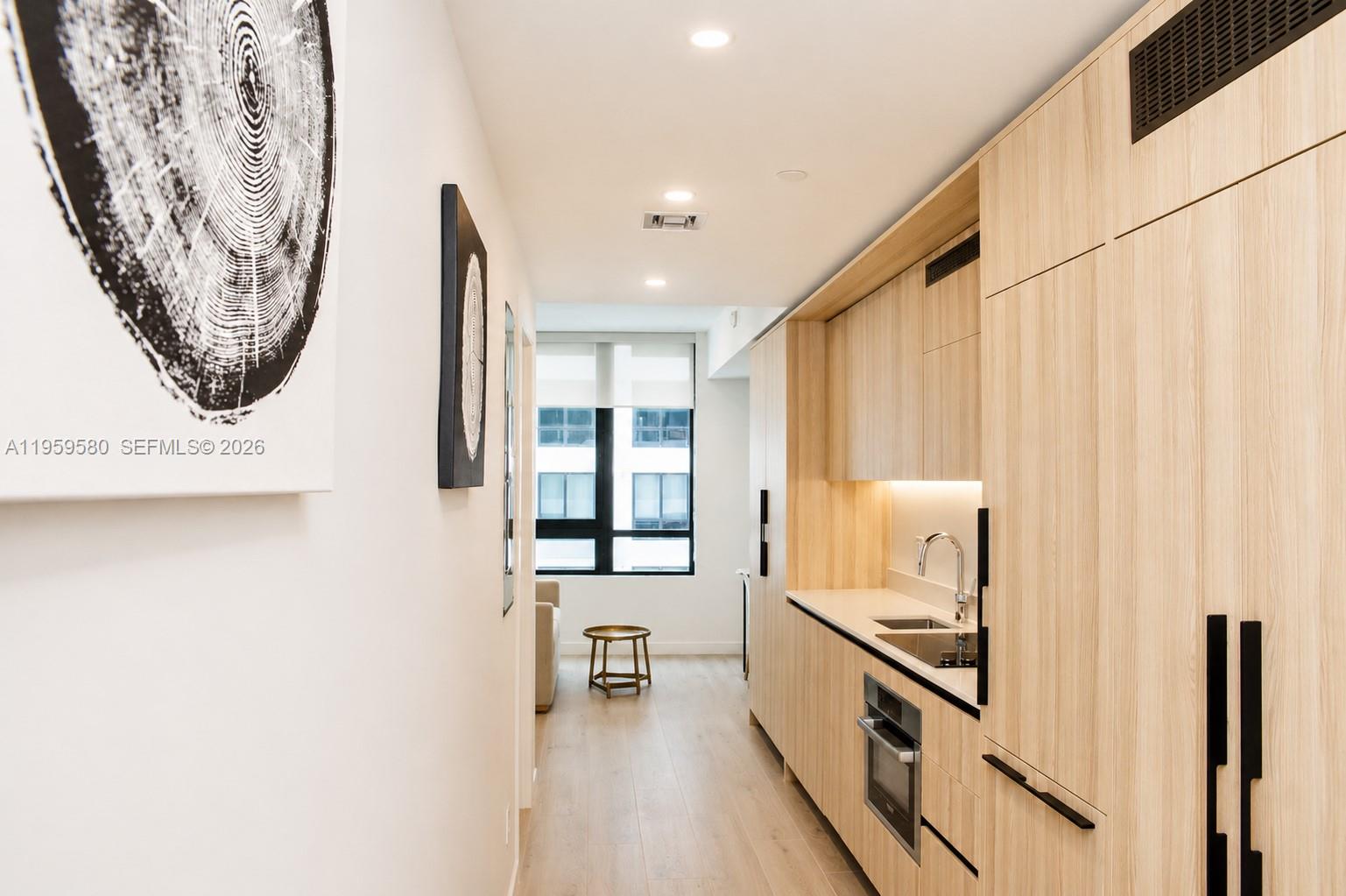 A narrow kitchen features light wood cabinetry, a stainless steel sink, and a built-in oven — 225 N Miami Ave # 2306, Miami FL 33128, MIAMI, FL