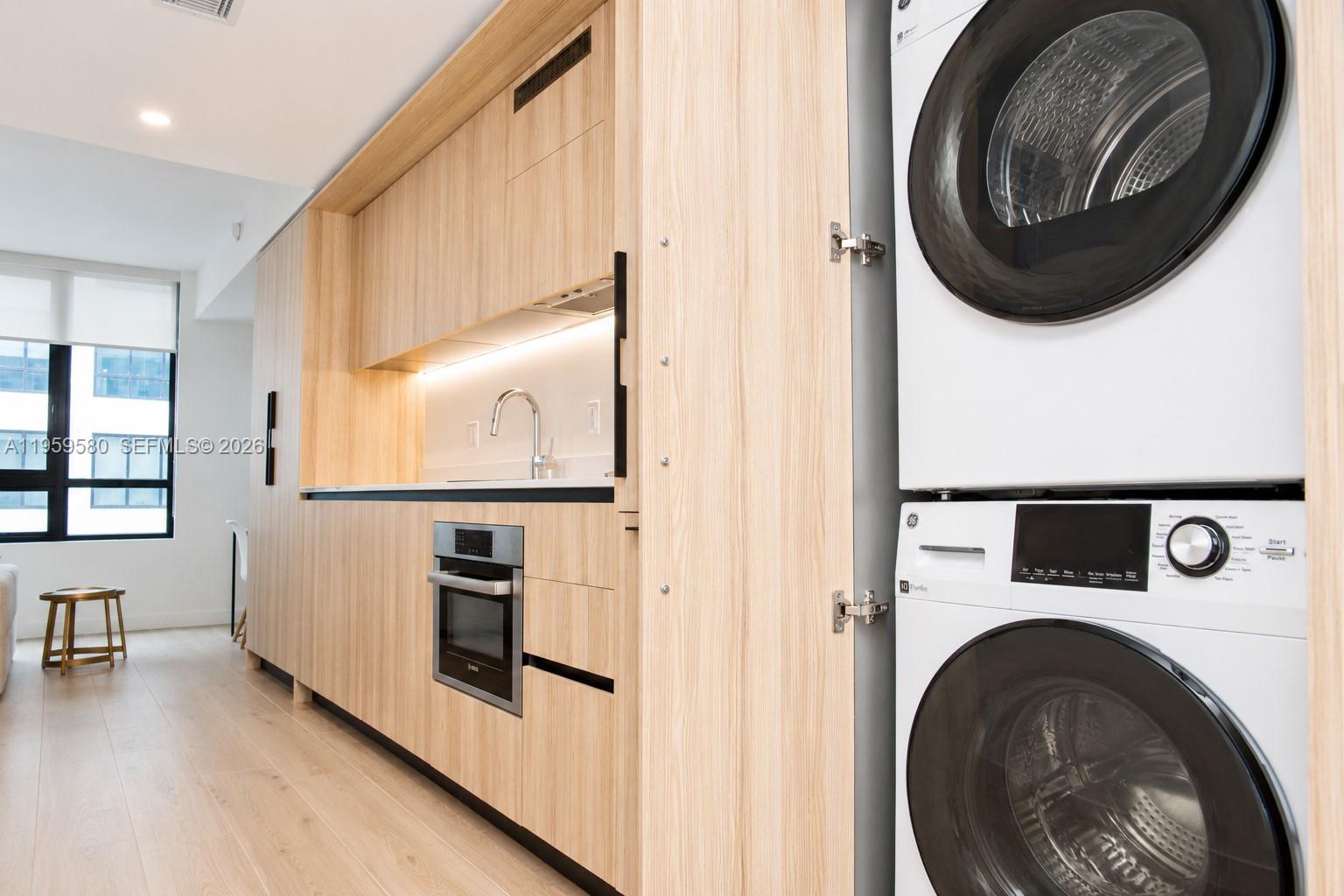 A modern kitchen features light wood cabinetry, a built-in oven, and a stacked laundry unit — 225 N Miami Ave # 2306, Miami FL 33128, MIAMI, FL
