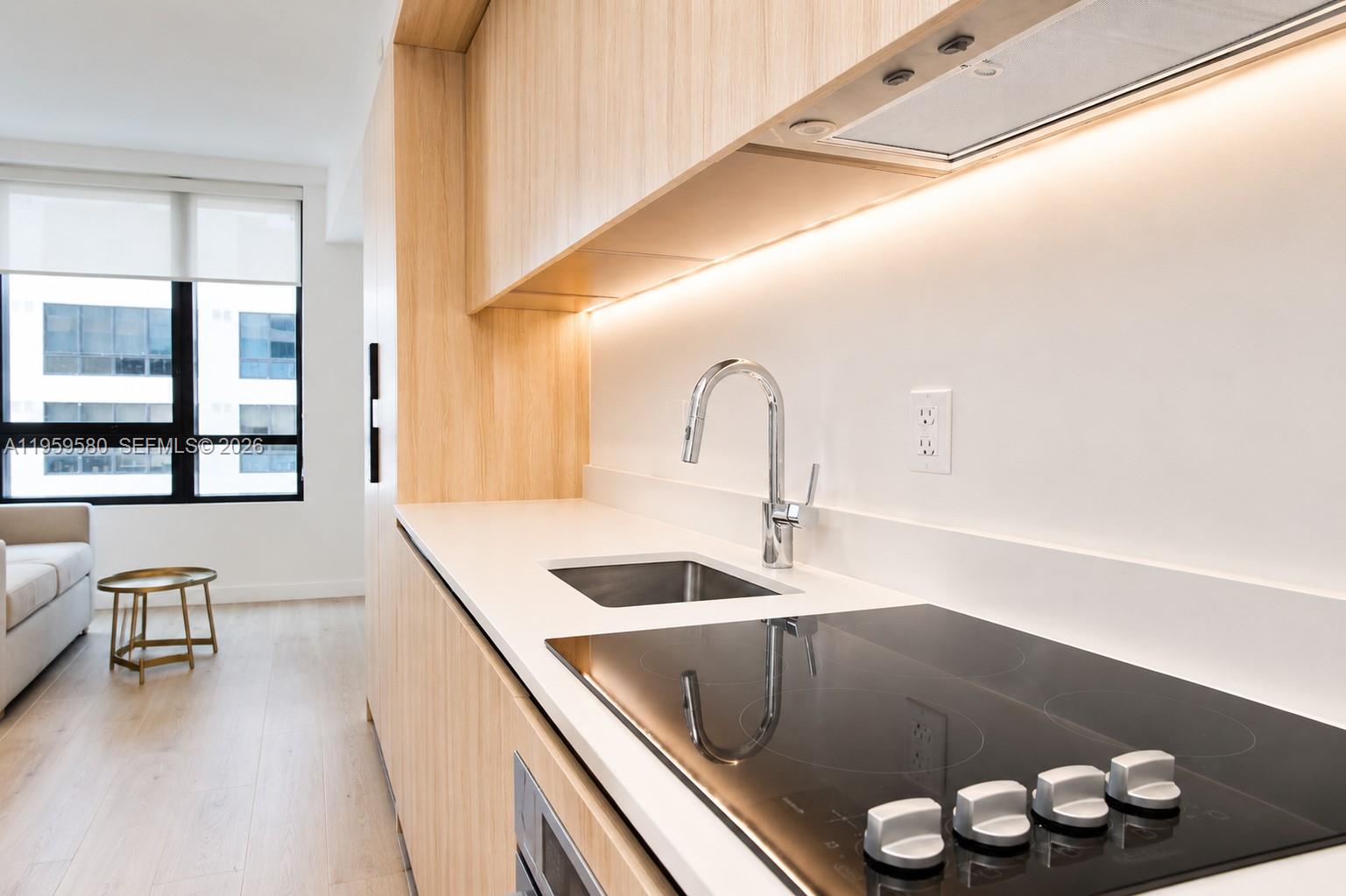 A modern kitchen features light wood cabinetry, a white countertop, and a black induction cooktop — 225 N Miami Ave # 2306, Miami FL 33128, MIAMI, FL
