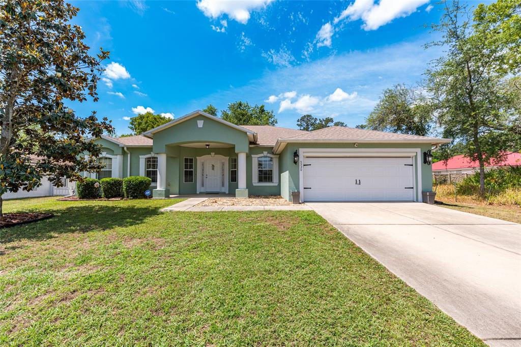 A single-story house with a green stucco exterior, a two-car garage, and a covered entryway — 5330 PECAN RD, OCALA, FL