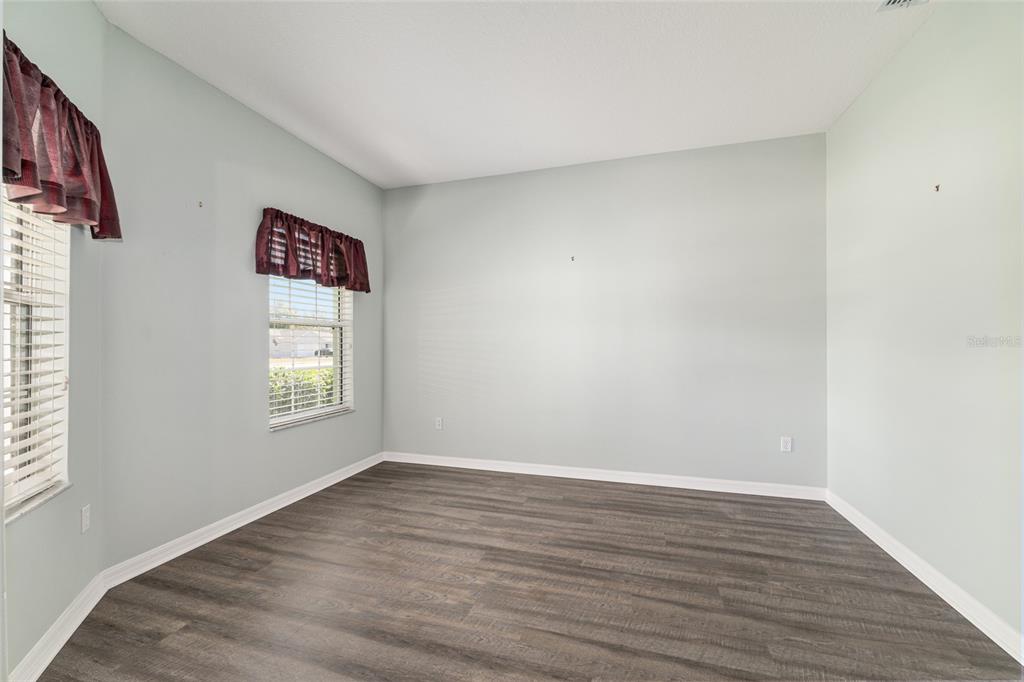 An empty room features light blue walls, dark wood-look flooring, and two windows with valances — 5330 PECAN RD, OCALA, FL
