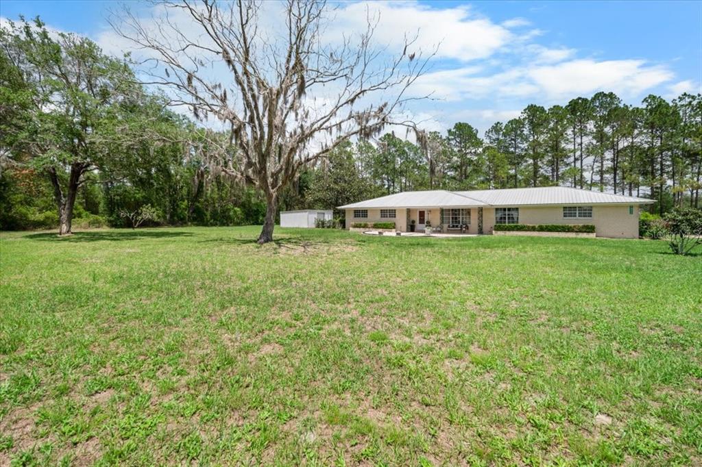 A single-story house with a metal roof sits on a large, grassy lot with trees — 7422 S COUNTY ROAD 231, LAKE BUTLER, FL