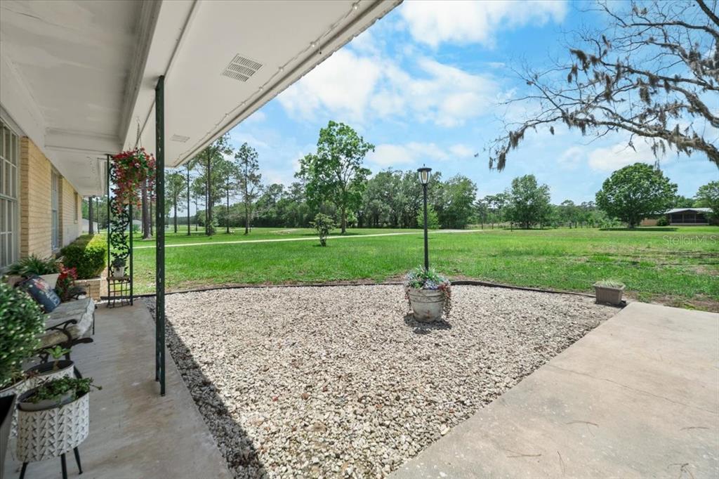 A covered concrete porch overlooks a gravel patio and a large, grassy backyard with trees — 7422 S COUNTY ROAD 231, LAKE BUTLER, FL