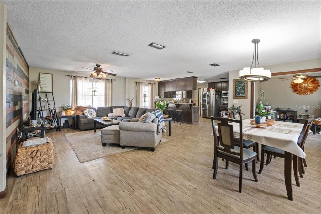 An open-concept living and dining area features wood-look flooring, a sectional sofa, and kitchen cabinetry — 7422 S COUNTY ROAD 231, LAKE BUTLER, FL