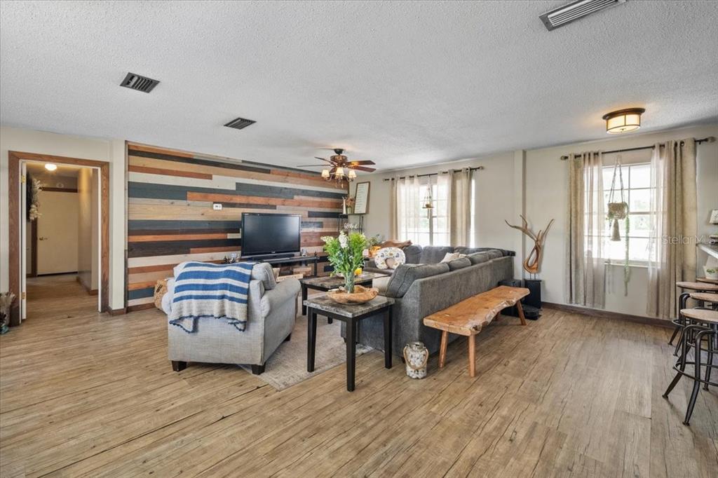 A living room features a wood-paneled accent wall, gray sectional sofa, and wood-look flooring — 7422 S COUNTY ROAD 231, LAKE BUTLER, FL