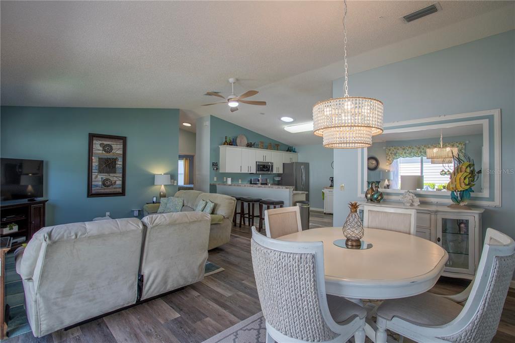 An open-concept living and dining area features light blue walls, wood-look flooring, and white furniture — 17403 SE 77TH SYCAMORE AVENUE, THE VILLAGES, FL