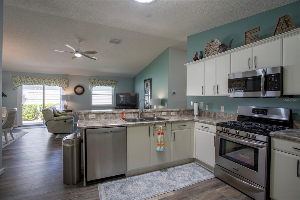A kitchen with white cabinets, stainless steel appliances, and a breakfast bar overlooking the living room — 17403 SE 77TH SYCAMORE AVENUE, THE VILLAGES, FL