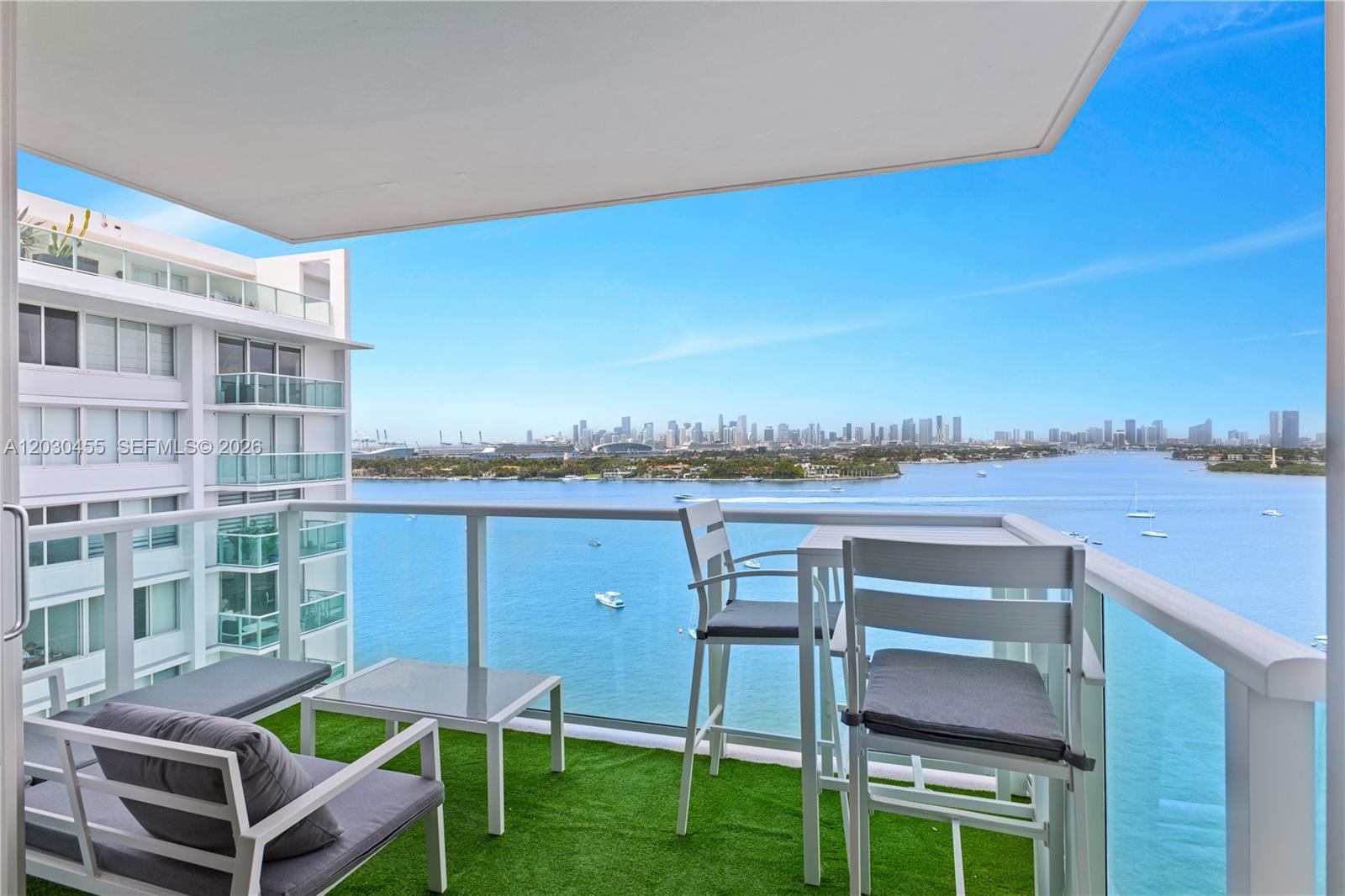 A balcony with artificial turf features outdoor furniture overlooking a bay and city skyline — 1000 West Ave # 1518, Miami Beach FL 33139, MIAMI BEACH, FL