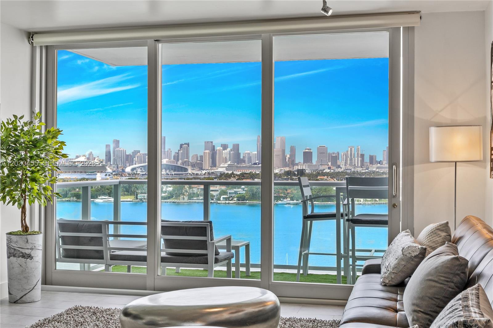 A living room with a sofa and floor-to-ceiling windows overlooking a balcony and city skyline — 1000 West Ave # 1518, Miami Beach FL 33139, MIAMI BEACH, FL