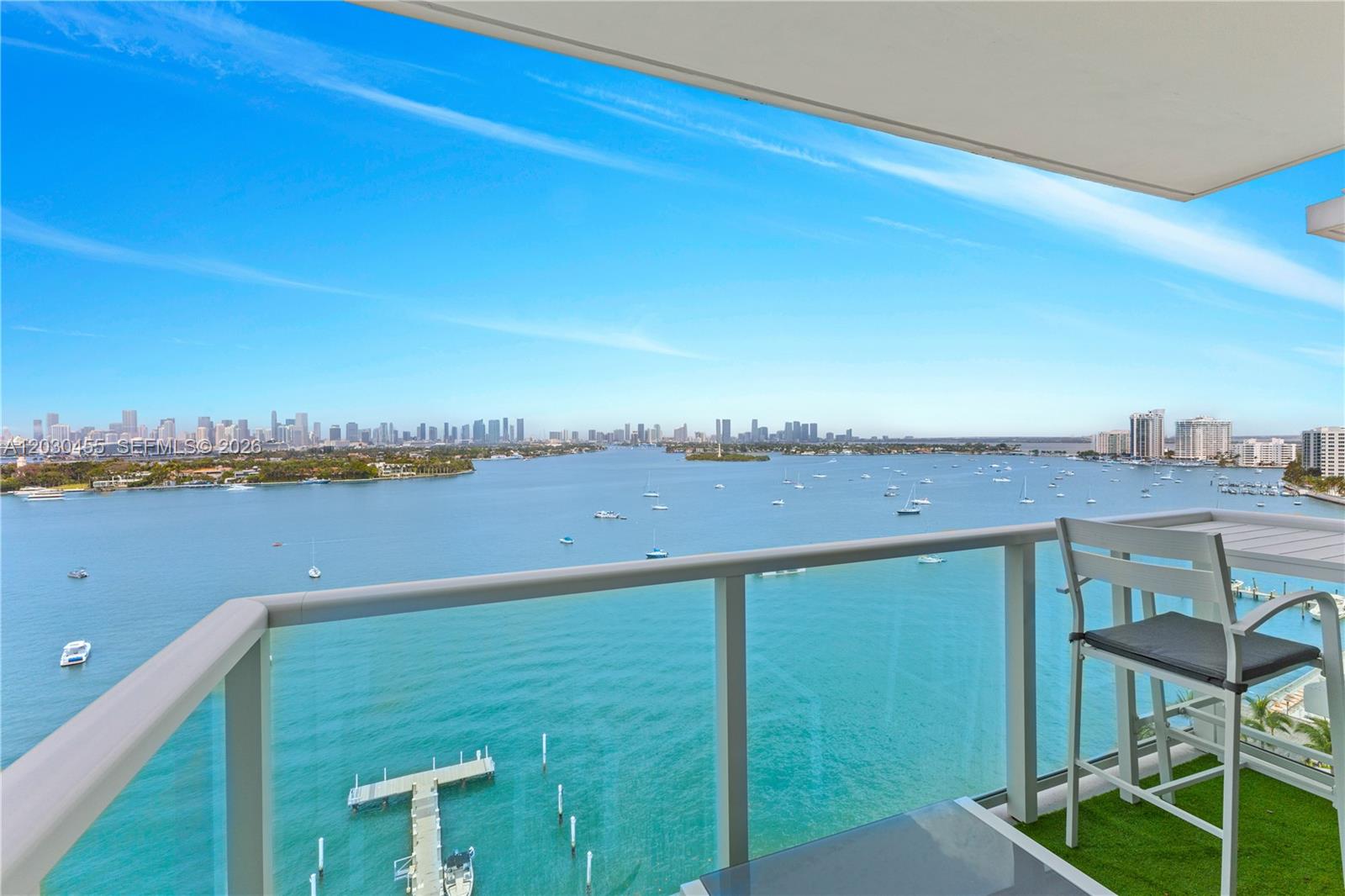 A balcony with a glass railing overlooks a bay with boats and a city skyline — 1000 West Ave # 1518, Miami Beach FL 33139, MIAMI BEACH, FL