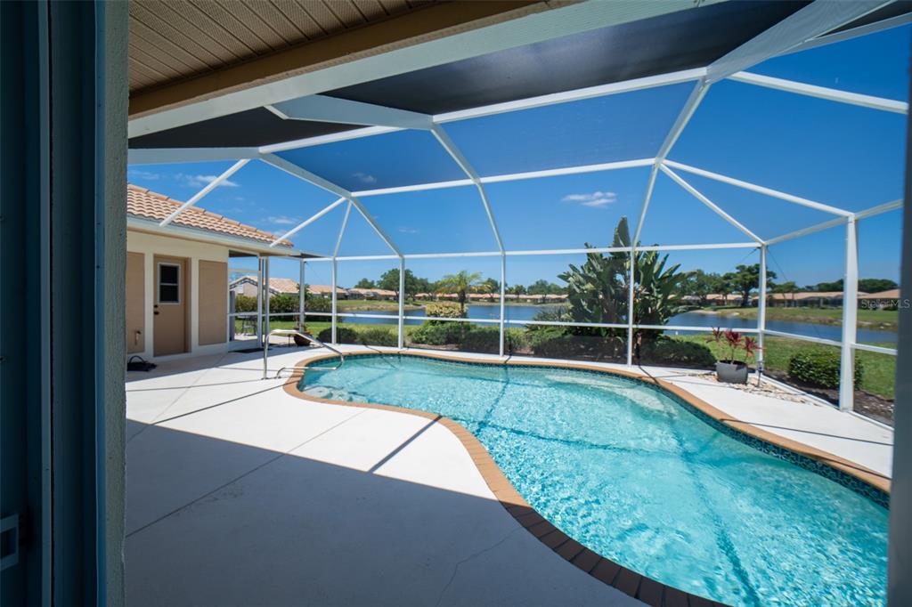 A screened-in patio features a kidney-shaped swimming pool overlooking a lake and residential neighborhood — 3162 E VILLAGE DRIVE, VENICE, FL