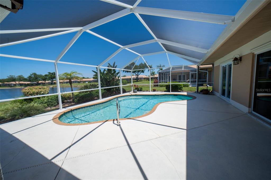 A screened-in patio features a kidney-shaped swimming pool overlooking a lake and residential neighborhood — 3162 E VILLAGE DRIVE, VENICE, FL
