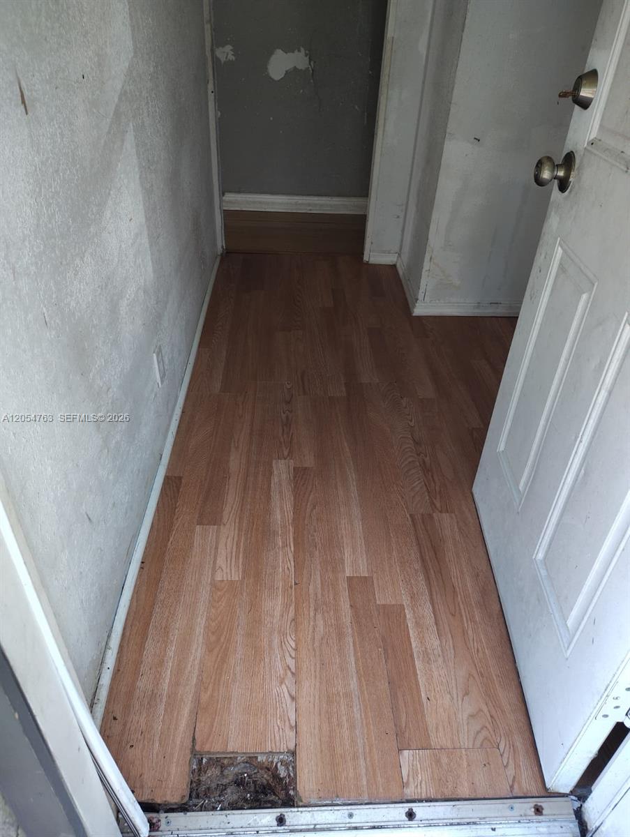 A doorway opens into a small room with wood-look laminate flooring and damaged wall surfaces — 26 Candlelight Dr, Lake Wales FL 33859, LAKE WALES, FL
