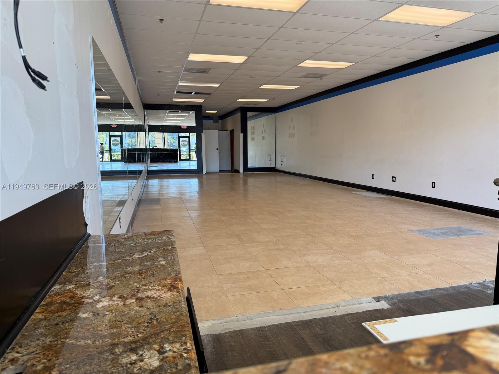 An empty commercial space features tan tile flooring, mirrored walls, and a granite countertop — 4570 Lyons Rd # 105, Coconut Creek FL 33073, COCONUT CREEK, FL