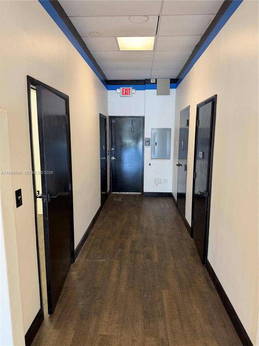 A narrow hallway features wood-look flooring, white walls, black doors, and a drop ceiling — 4570 Lyons Rd # 105, Coconut Creek FL 33073, COCONUT CREEK, FL