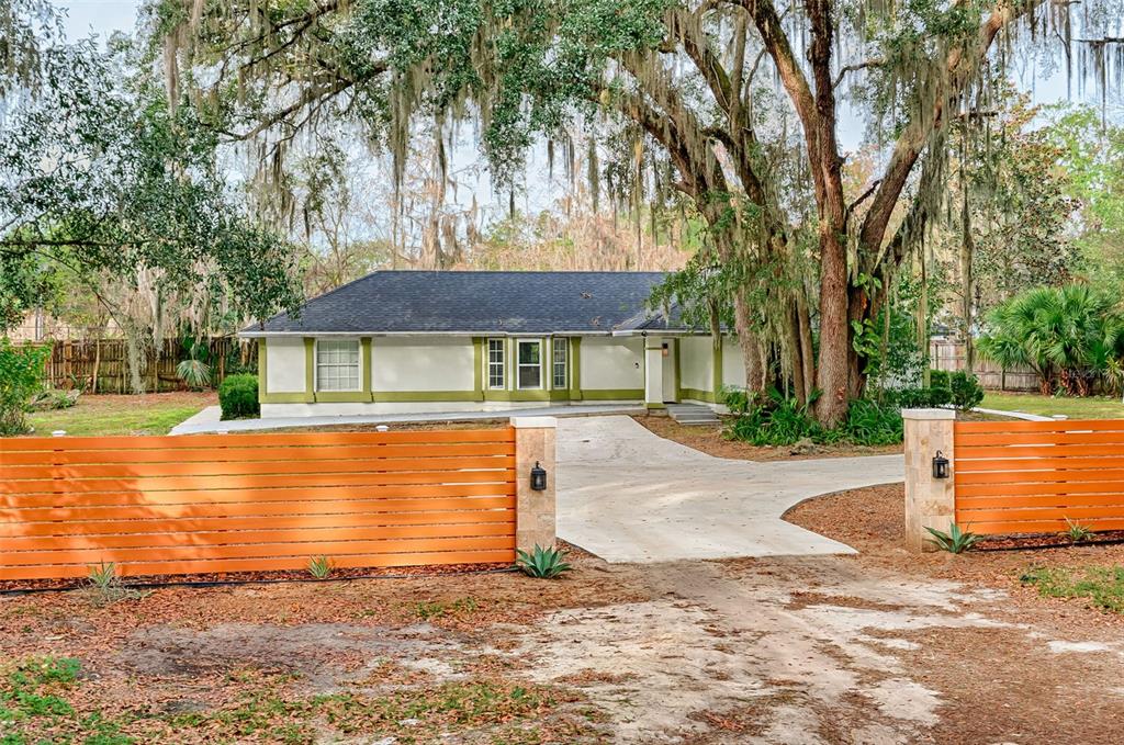 A single-story house with a white facade and green trim sits behind an orange fence — 3222 SW 27TH STREET, GAINESVILLE, FL