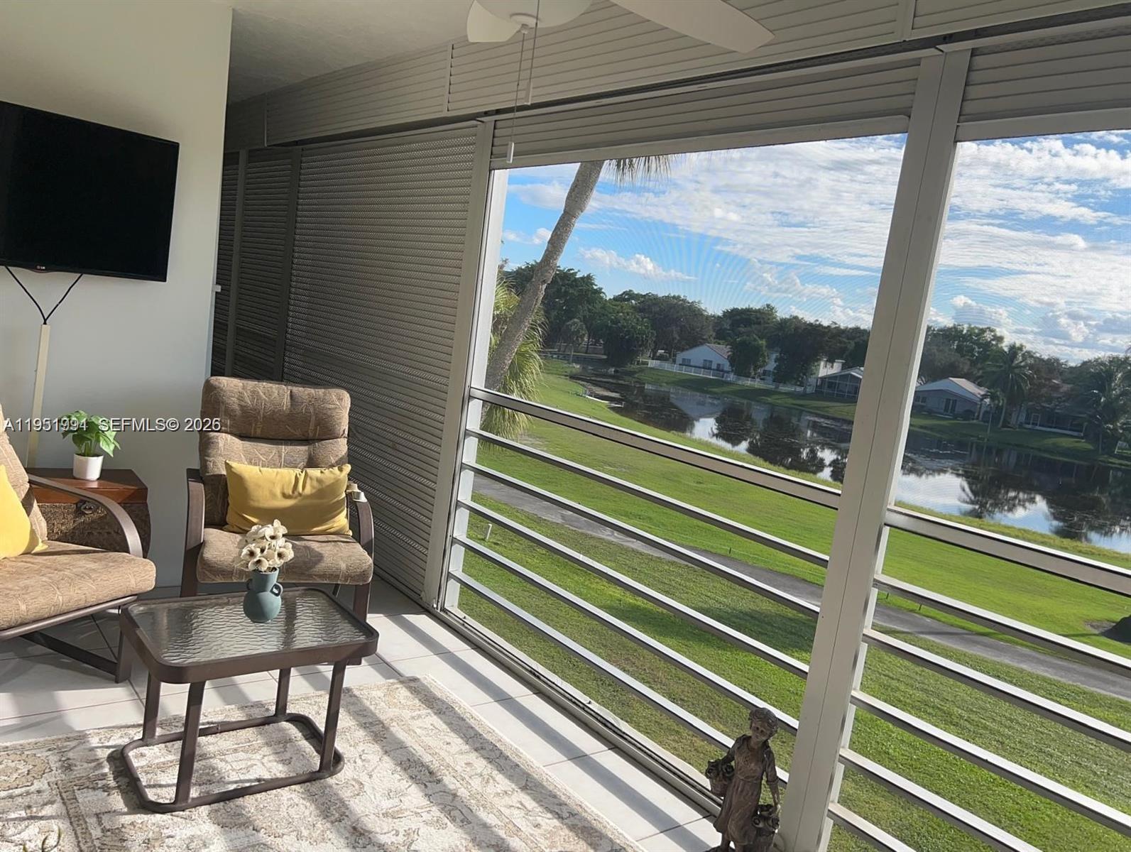 A sunroom with chairs, a table, and a screen wall overlooking a pond and lawn — 821 Cypress Blvd # 312, Pompano Beach FL 33069, POMPANO BEACH, FL