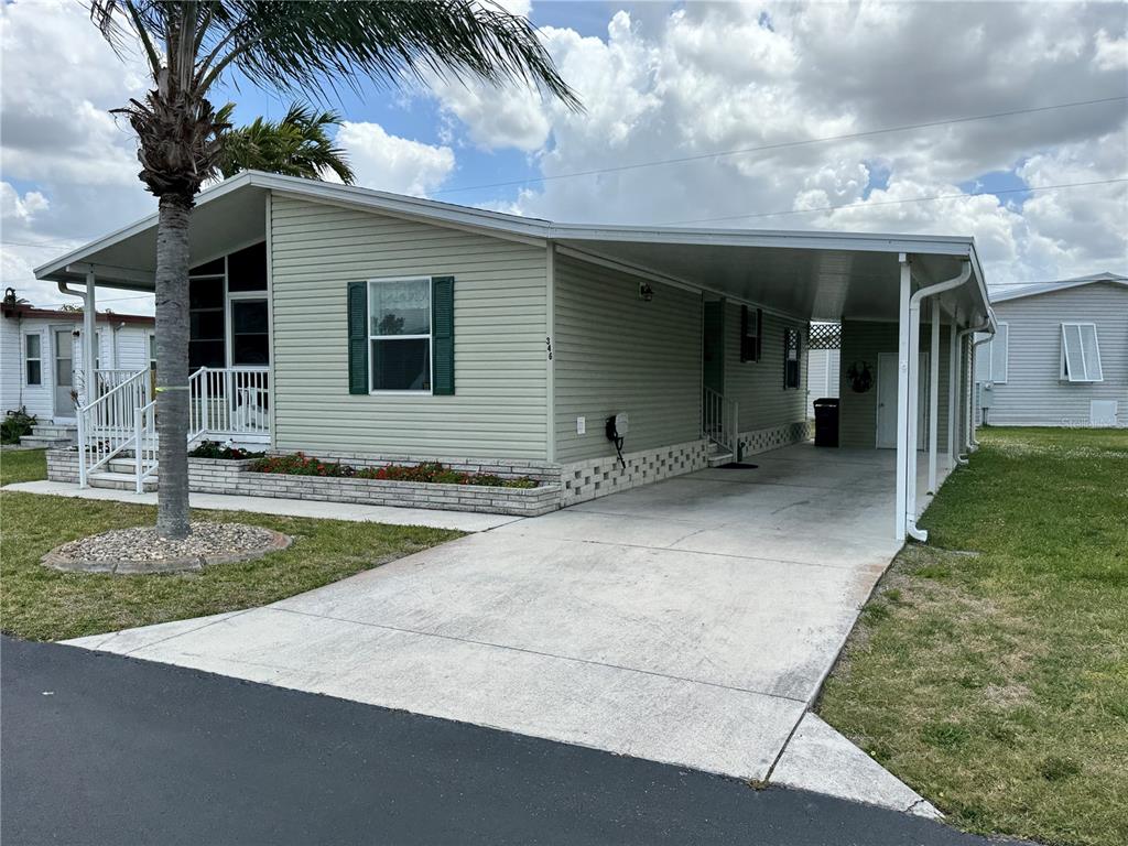 A light green mobile home features a concrete driveway, a carport, and a front porch — 346 ANDROS DRIVE, SARASOTA, FL