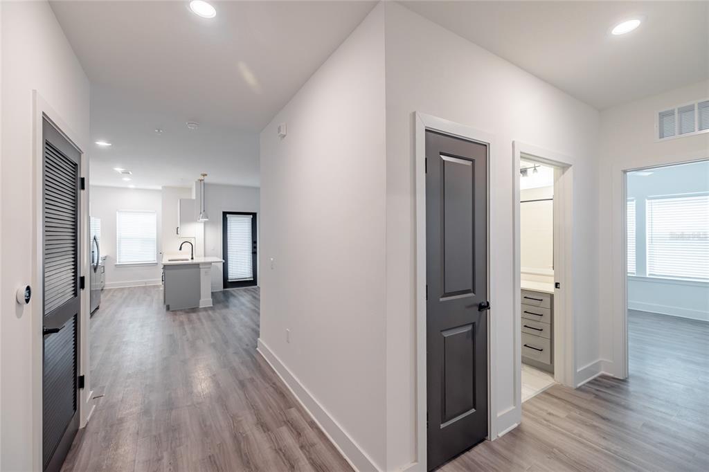 A hallway with light wood-look flooring leads to a kitchen and two rooms with doors — 1420 LAKEFRONT DRIVE UNIT 7111, SARASOTA, FL