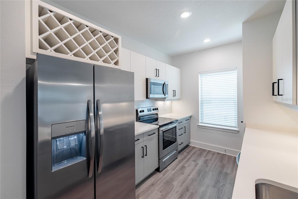 A modern kitchen features stainless steel appliances, white cabinetry, a wine rack, and wood-look flooring — 1420 LAKEFRONT DRIVE UNIT 7111, SARASOTA, FL