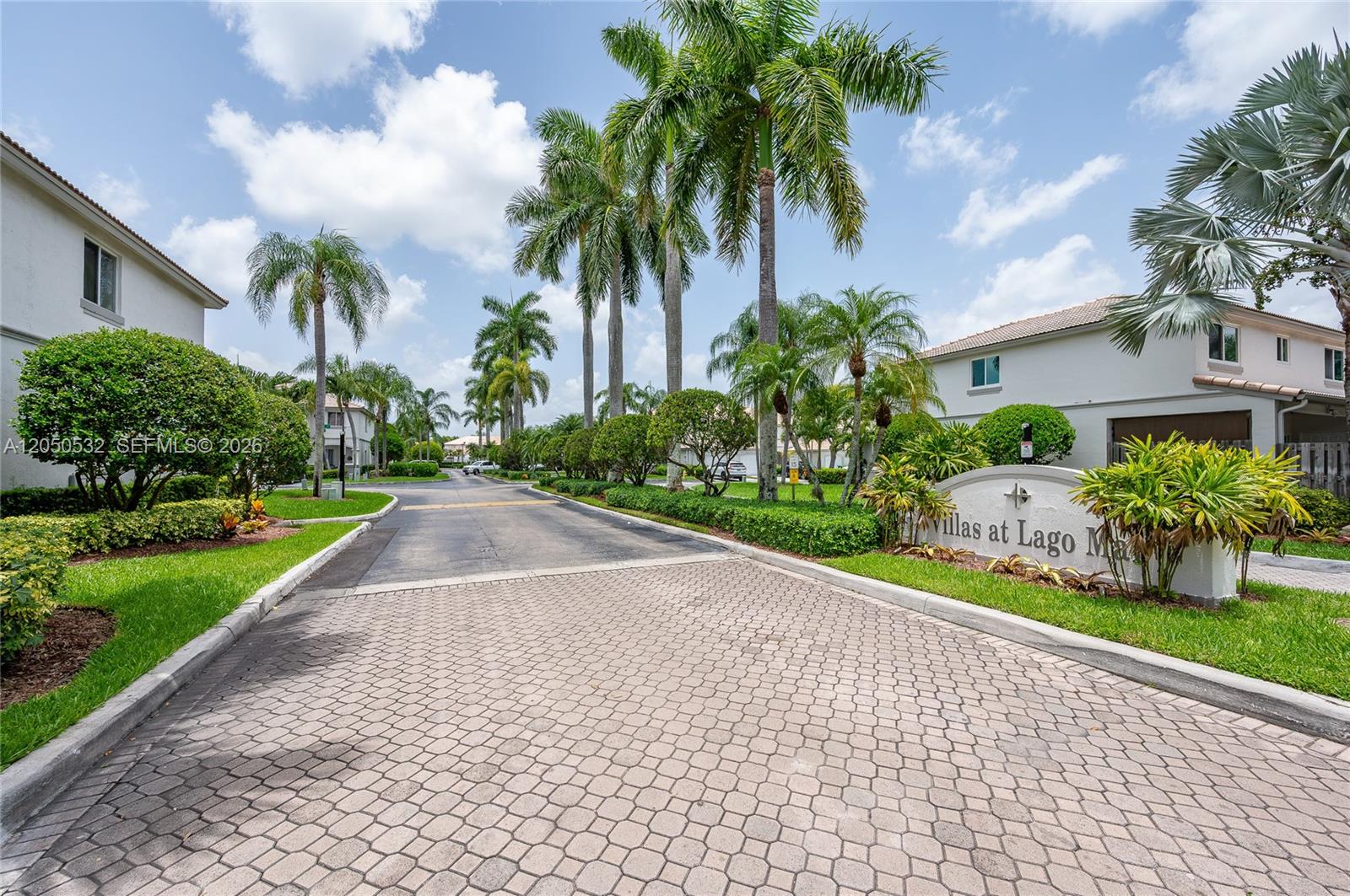 A paved driveway leads into a residential community with palm trees and a stone sign — 7240 SW 162nd Ct, Miami FL 33193, MIAMI, FL