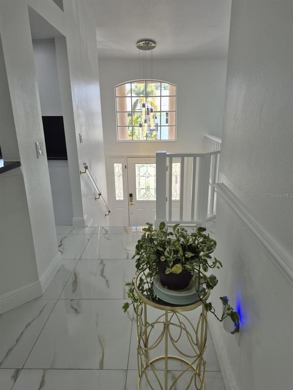 An elevated view of a foyer with white marble-style flooring, a staircase, and a front door — 5451 TROPIC DRIVE, NEW PORT RICHEY, FL