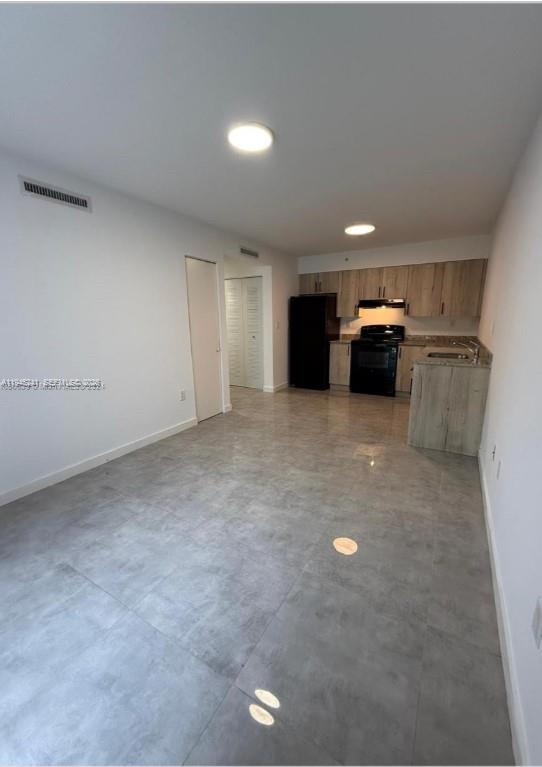 A kitchen with light wood cabinets and a black stove opens into a tiled living area — 14752 NE 6th Ave # 305, Miami FL 33161, MIAMI, FL
