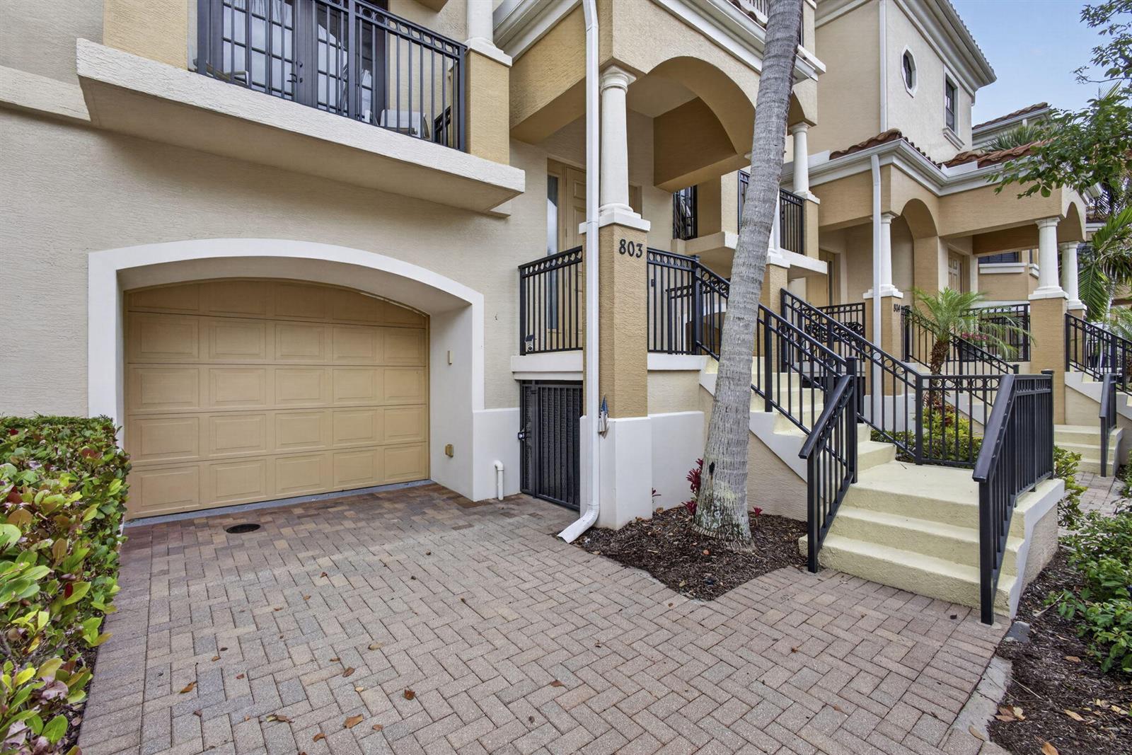 A multi-story townhouse exterior features a tan garage, brick driveway, and a staircase leading upward — 803 Del Sol Circle, Tequesta FL 33469, TEQUESTA, FL