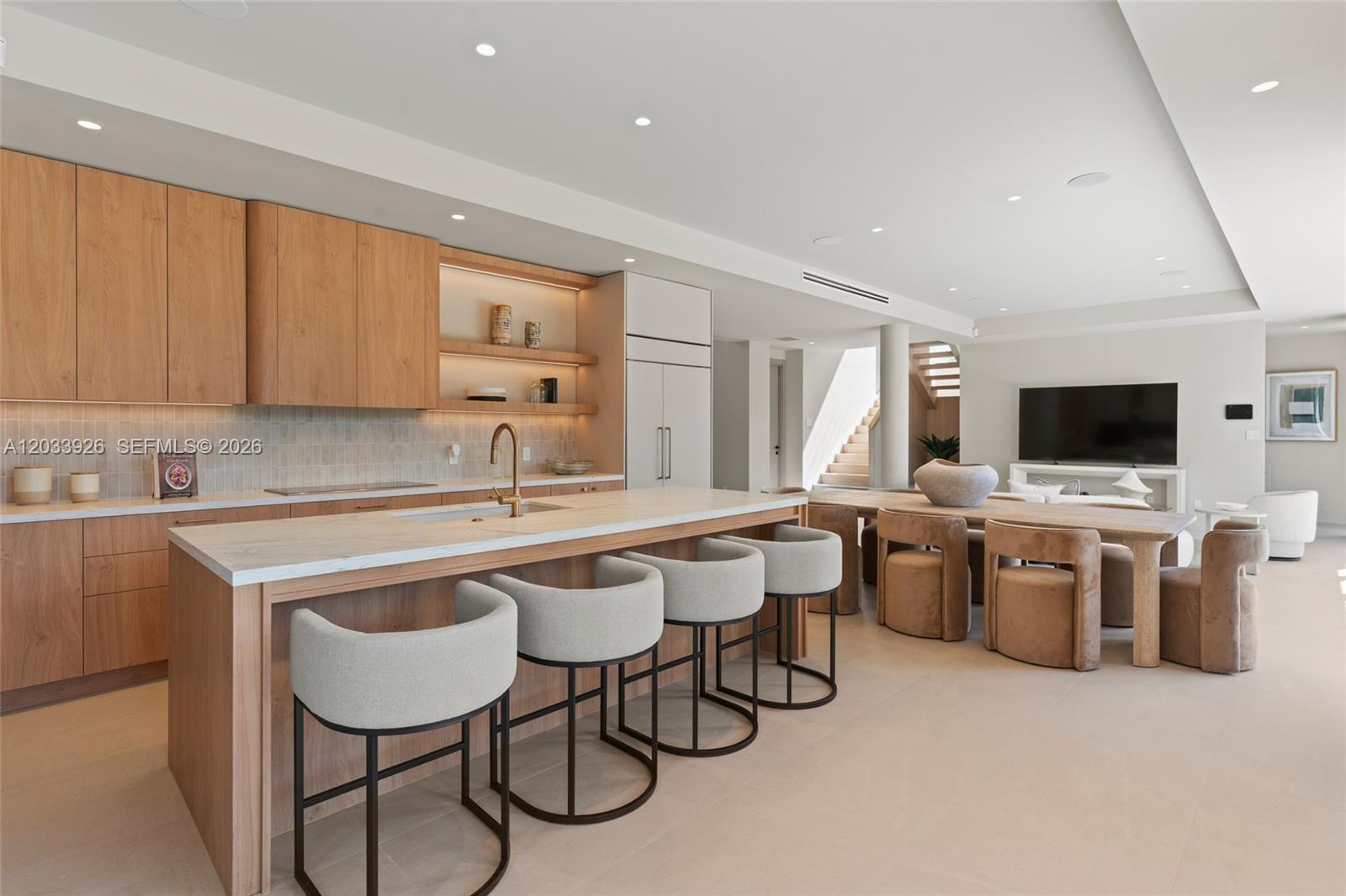 A modern kitchen features light wood cabinetry, a marble island with bar stools, and dining area — 5854 SW 30th St, Miami FL 33155, MIAMI, FL