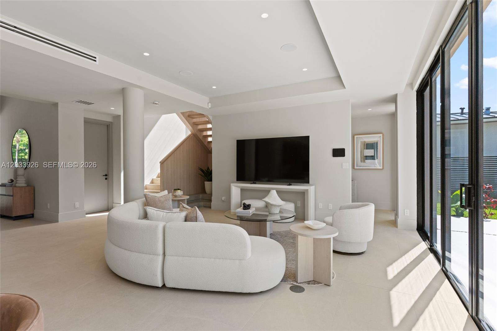 A modern living room features a curved white sofa, glass coffee table, and large windows — 5854 SW 30th St, Miami FL 33155, MIAMI, FL