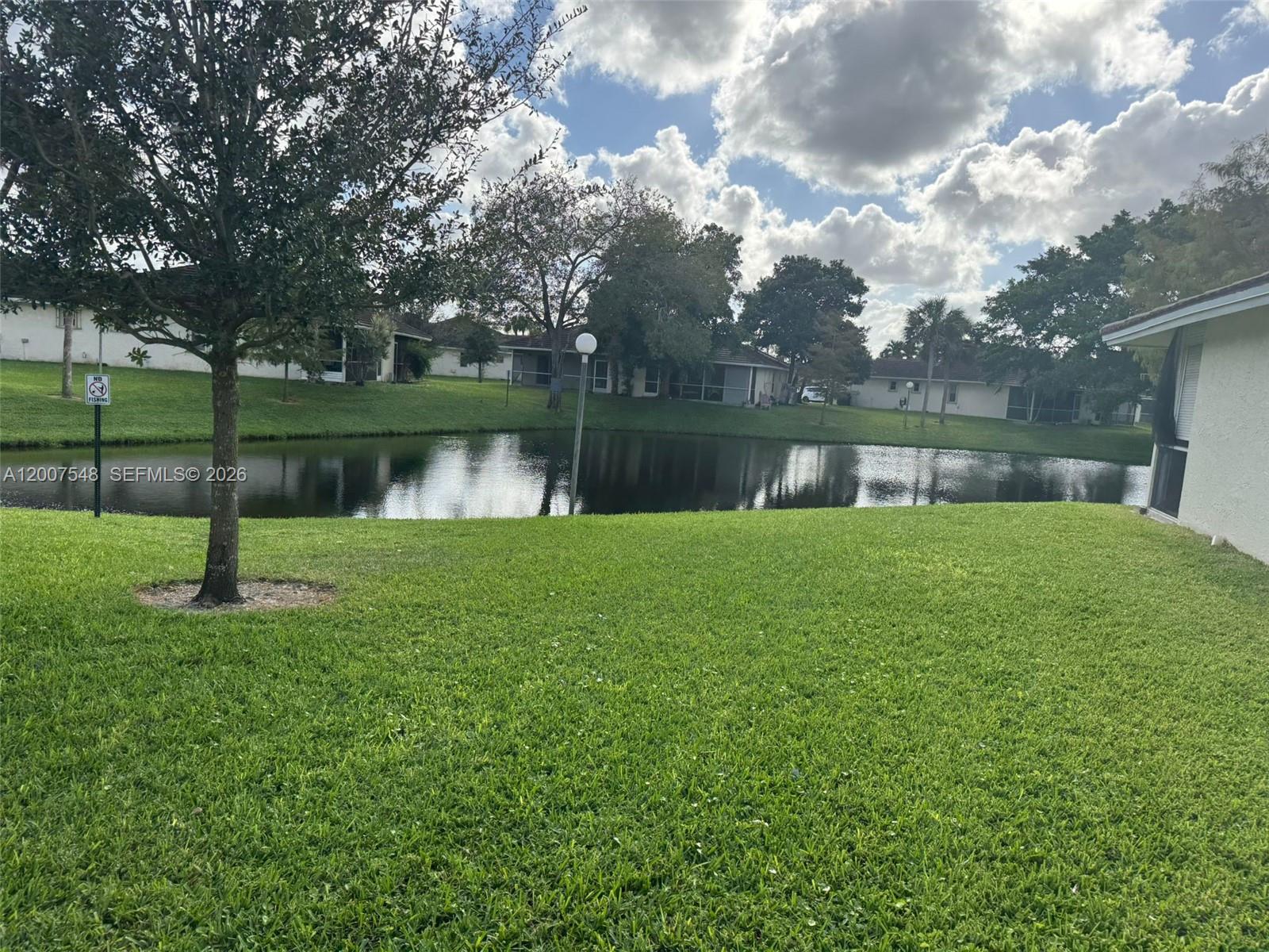A grassy backyard overlooks a small pond surrounded by trees and residential houses — 9863 Three Lakes Cir, Boca Raton FL 33428, BOCA RATON, FL