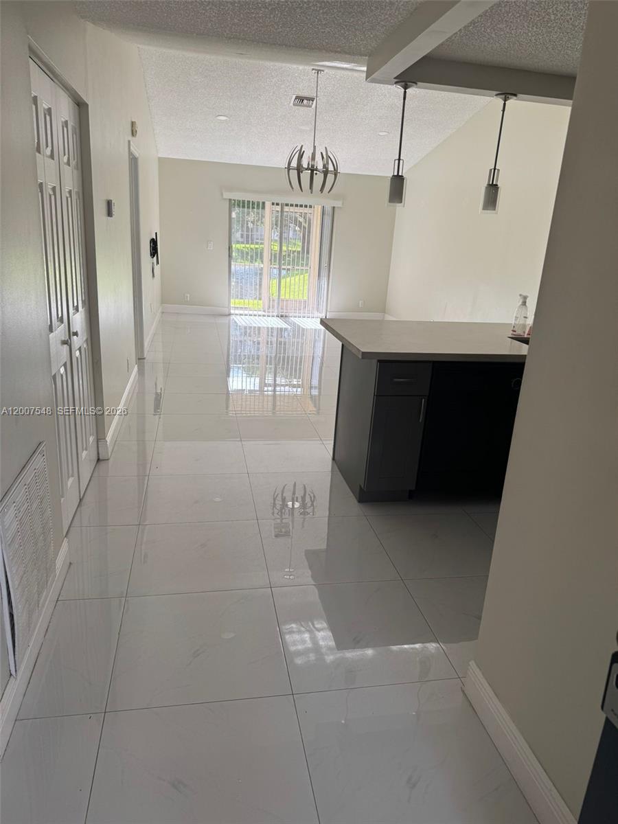 A bright room features white tile flooring, a kitchen island, and sliding glass doors — 9863 Three Lakes Cir, Boca Raton FL 33428, BOCA RATON, FL