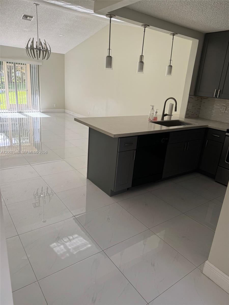A kitchen with dark cabinets and a light countertop overlooks a bright, tiled living area — 9863 Three Lakes Cir, Boca Raton FL 33428, BOCA RATON, FL