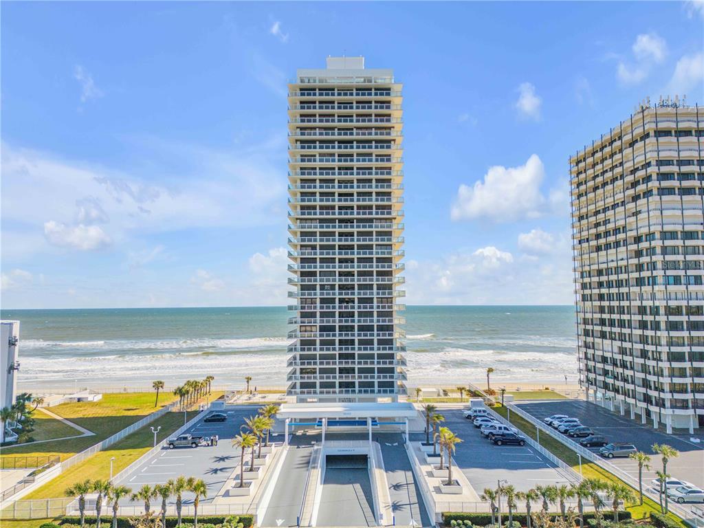 An exterior view of a tall beachfront condominium building with a parking lot in front — 3000 N ATLANTIC AVENUE UNIT 18, DAYTONA BEACH, FL