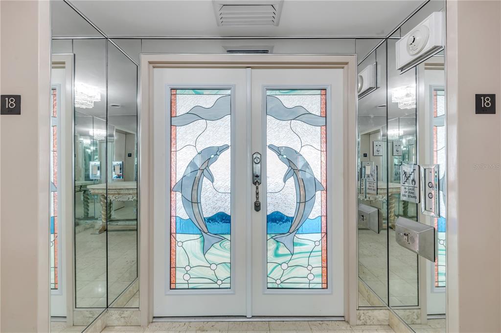A double door with stained glass dolphin panels sits between mirrored walls in a hallway — 3000 N ATLANTIC AVENUE UNIT 18, DAYTONA BEACH, FL