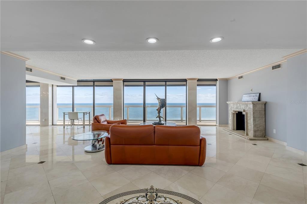 A spacious living room features marble floors, a fireplace, and floor-to-ceiling windows overlooking the ocean — 3000 N ATLANTIC AVENUE UNIT 18, DAYTONA BEACH, FL